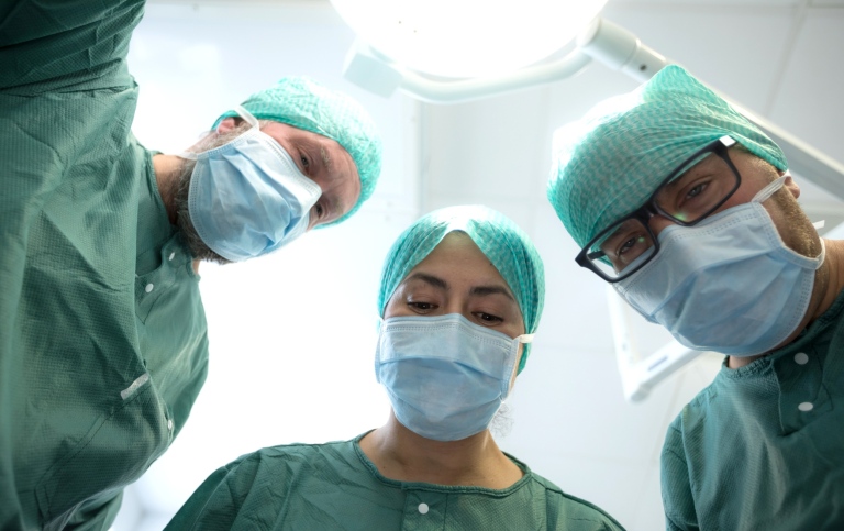 Three surgeons dressed in green are leaning over the camera. 